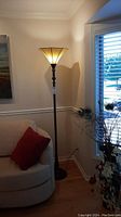 Full view of the torchier floor lamp illuminated beside a couch with a red pillow and window with blinds