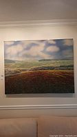 Full frontal view of landscape canvas painting on metal frame mounted on wall above sofa