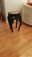Full view photo showing the octagonal marble top and carvings on dark wooden base of the side table placed on a hardwood floor.