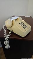 Side view of off-white vintage Northern Telecom push button landline phone showing handset, keypad, and coiled cord.