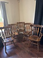 Front and side view of five solid wooden armchairs grouped together on a hardwood floor with curtains in background.