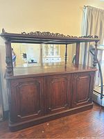Full view of antique wooden hutch showing carved top trim, three-paneled cabinet doors, and turned side columns.