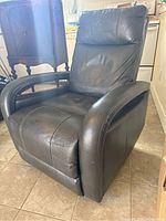 Dark brown faux leather swivel recliner rocker chair angled showing seat, armrest, and base on tiled floor.