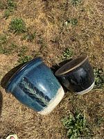 Two blue clay plant pots seen from top down on dry grass showing exterior design and glaze.