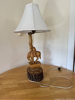 Full view of carved cowboy lamp with white fabric lampshade and wooden base placed on wooden surface.