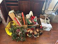 Photo showing assorted Christmas decorations including wreaths, ribbons, holiday figurines, lighted reindeer figure, and various items in boxes and bags.