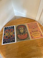 Three 17x11 inch vintage concert posters placed side by side on a wooden table, each in plastic protector, showing colorful psychedelic and portrait art.