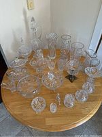 Full view of 24 lead crystal glassware pieces arranged on a wooden table showing a variety of glasses, vases, decanter, and bowls with detailed hand cut designs.