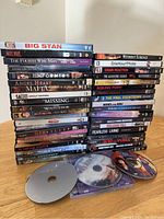 Photo showing a stack of assorted DVD movies with titles and some loose discs at front.
