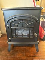 Front view of black electric stove with glass window door and spring handle latch, showing the decorative arched window design.