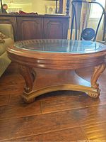 Side view of the round coffee table showing wooden carved legs and thick glass top.