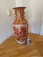 Full view of the large porcelain vase with red, gold, and white floral and scenic decorative artwork, placed next to a soda can for size reference.