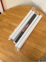 Five rolled posters in plastic sleeves on a wooden round table, mostly white rolled sleeves with one black.