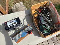 Wide photo showing wooden box with assorted tools and other loose items on a table outdoors