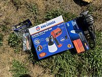 Items laid out on grass showing an electric spray gun box King Canada, electric rotary sander in blue/black, paint brushes in package, and sanding supplies.