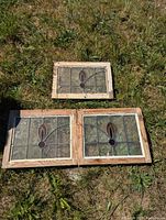 Three stained glass window panels with wooden frames placed on grass, showing their worn and weathered condition.