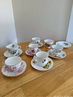 Photo of all six tea cup and saucer sets arranged on a wooden table showing varying floral patterns.