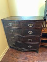Front view of the curved dresser showing four drawers and metal pulls, showing wear on the bottom edges.