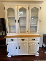 Front view of white wooden cabinet with upper glass doors and lower cabinets with drawers.