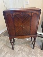 Front view of wooden cabinet with chevron veneer pattern and ornate handles