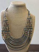 Front view of vintage Bohemian metal and bead necklace on beige display bust showing layered curved metal tubes and multi-colored beads.