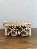 Side view of underside of miniature wicker table showing woven structure and legs tied with string.