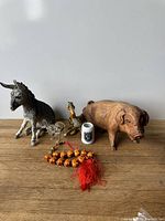 Front view of the lot showing hand carved wooden pig, painted donkey, ceramic pelican, crystal elephant, ceramic thimble, and bead tassel on white surface