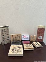 Photo of assorted wooden block stamps and ink pads arranged on table, showing floral, text, butterfly, and other craft designs.