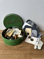 Top view of open round vintage Katherine Beecher tin showing assorted buttons and sewing ephemera inside.