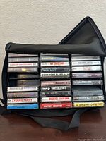 Photo of vintage cassette tapes stacked in black soft case, showing titles and artist labels of 24 tapes including Michael Jackson and Whitney Houston.