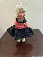 Front view of vintage Dutch doll showing facial features, lace bonnet, red and floral bodice, black apron, and white wooden shoes.