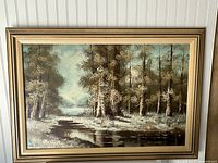 Full view of the framed vintage forest scene oil painting showing trees, water reflection, and natural colors.
