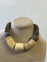 Front view of the vintage tribal necklace on display stand showing large central curved bead and numerous flat round cream colored carved beads.