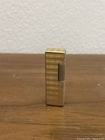 Front view of a vintage gold tone rectangular lighter with textured surface and ignition wheel on side.