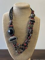 Photo of vintage Tibetan necklace displayed on beige fabric bust, showing full front view with asymmetrical bead design and ornate centerpiece.