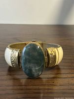 Front view of bracelet showing large oval green stone centerpiece mounted on gold-tone metal band with mother of pearl inlays.