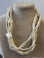 Full view of the vintage white multi-strand necklace displayed on a bust, showing multiple strands and elephant pendants.