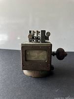 Front view of compass showing rectangular glass window and mechanical adjustment components on top with adjustment knobs.