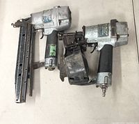Two used pneumatic nailers, one smaller NV 45AB2 and one larger NV 65A3, placed side by side on a surface showing wear and rust.