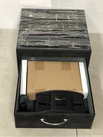 Closed black leather case with organized compartments inside containing cardboard and styrofoam pieces, wrapped items.