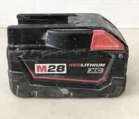 Side view of Milwaukee M28 REDLITHIUM XC battery pack showing model and branding with signs of wear.