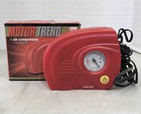 Motor Trend CPM-0160 compact red air compressor with pressure gauge on front, power cord coiled next to device, original box behind it with visible branding and model info.