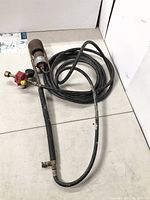 Full propane torch assembly with hose and burner head, coiled on floor.