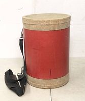 Side view of the drum showing red body, natural drum heads and black carrying strap.