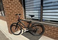 Full side view of the black Shimano Sportek bicycle leaning against a brick wall outdoors, showing overall condition and components.