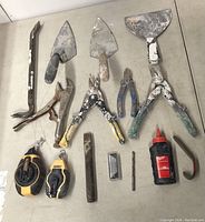 Top-down image showing a variety of used hand and garden tools on a white surface, with paint residue on several tools.