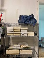 Metal shelving with a blue duffel bag on top shelf, cardboard card boxes below