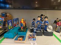 Photo shows Beatles figurines, baseball coin throw game, playing cards, and coasters arranged together