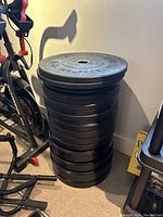 Stack of 17 black Bells of Steel plates leaning against wall alongside exercise equipment