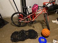 Coral pink Cannondale Quick kids bicycle parked on concrete floor with helmet on handlebars, basketball and disc nearby